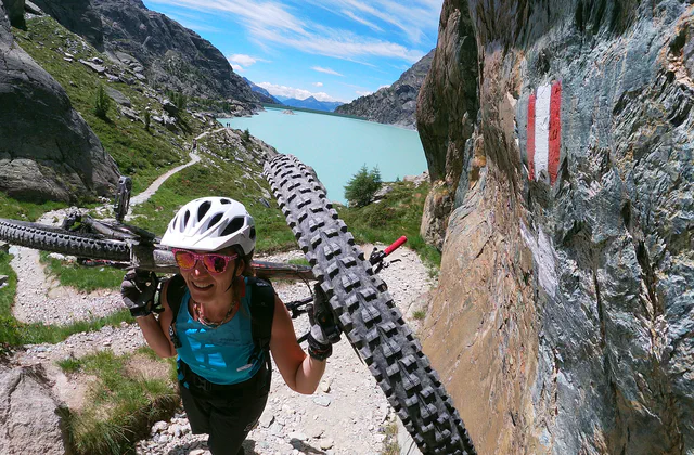 Mountain biker carrying a bike on a trail in Valmalenco